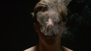 Male blowing out smoke from his mouth with a black background