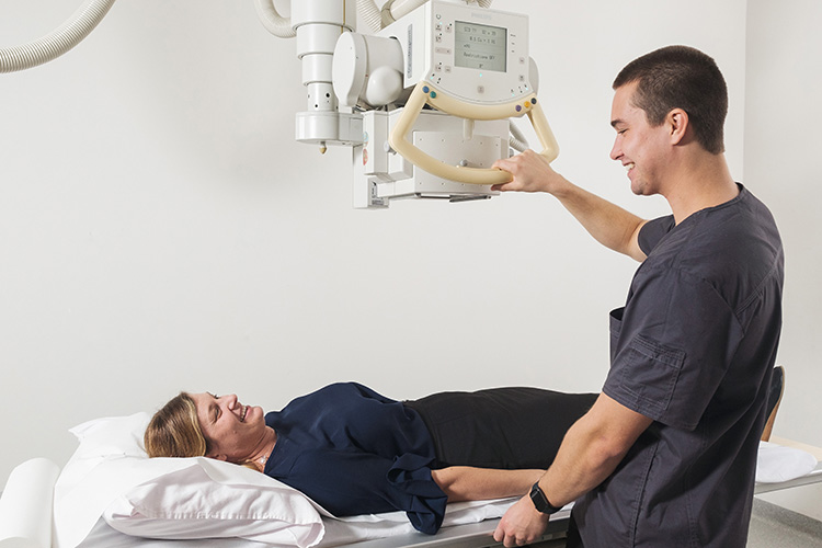 Female patient lying down on a table with a male doctor holding an X-Ray machine over her