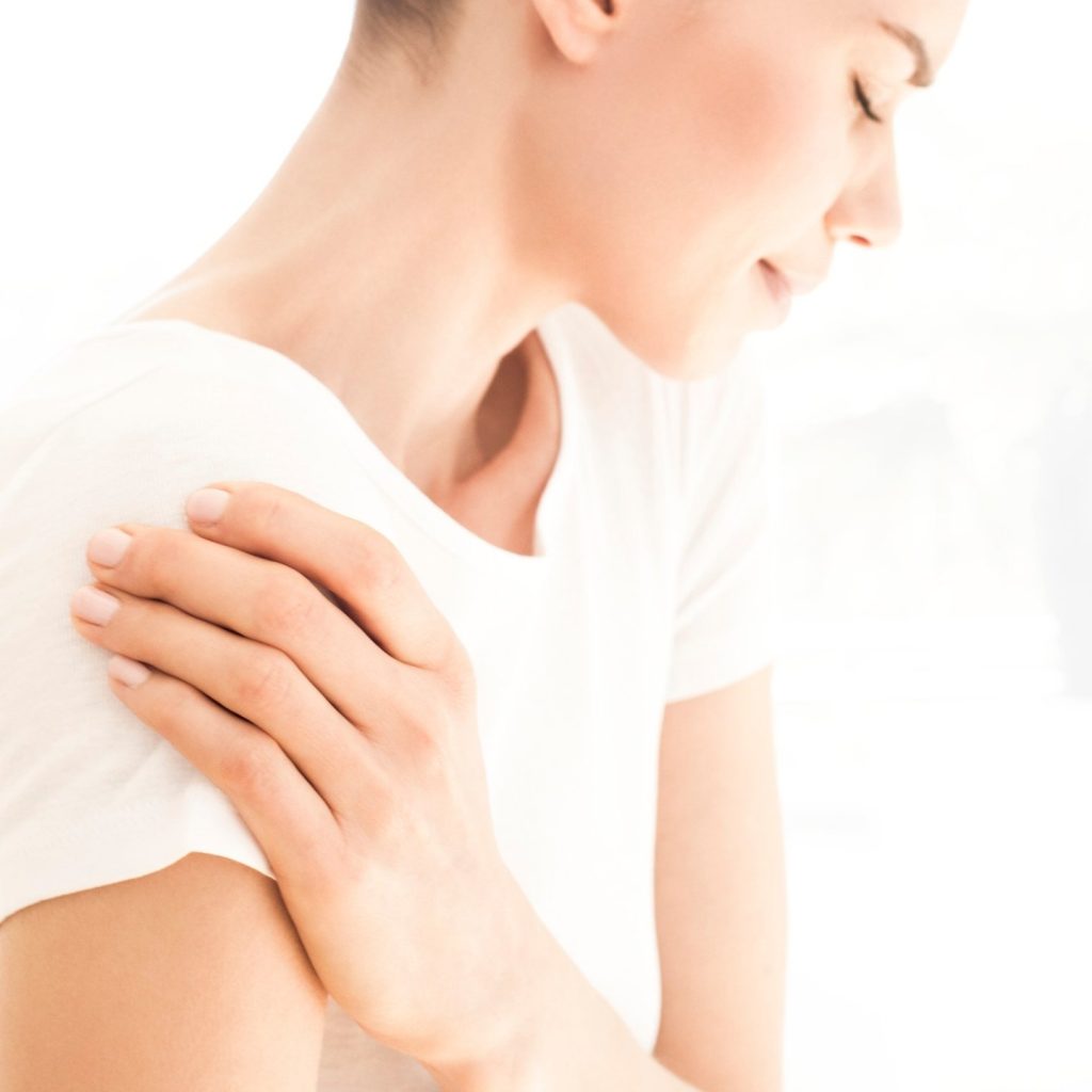 Woman in white T-shirt holding her shoulder because of shoulder pain