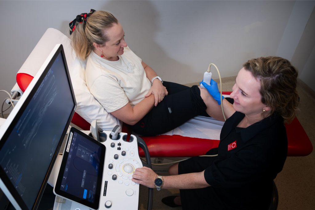 Ultrasonographer does knee ultrasound on female patient to investigate pain